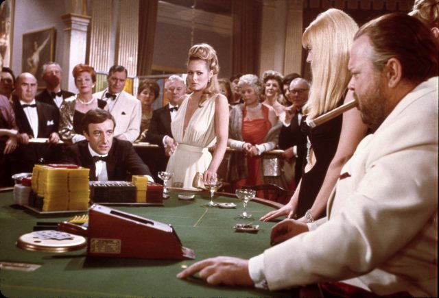 Group of people surrounding James Bond as he plays baccarat in scene from 1967 Casino Royale