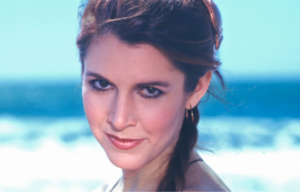 Carrie Fisher smiles at the camera over her shoulder on the beach