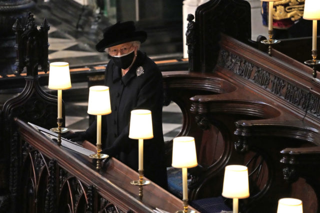 Queen Elizabeth II, wearing a mask, watches as pallbearers carry the coffin of Prince Philip