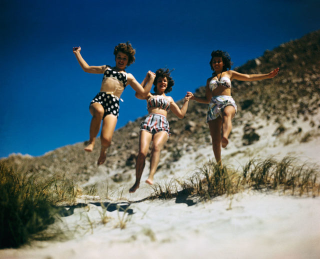 Three young women run to the shore in their swimming outfits