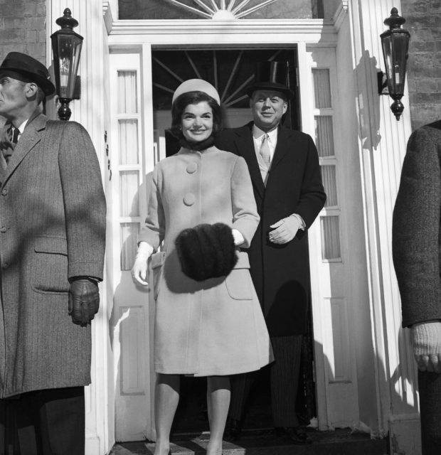 Jackie Kennedy heading for the White House wearing pill box hat and A-line coat with husband John F. Kennedy behind her