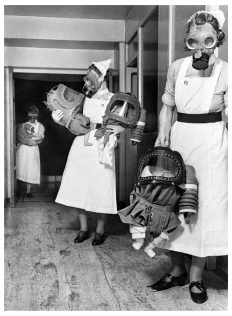 Nurses carry infants in large gas masks during WWII.