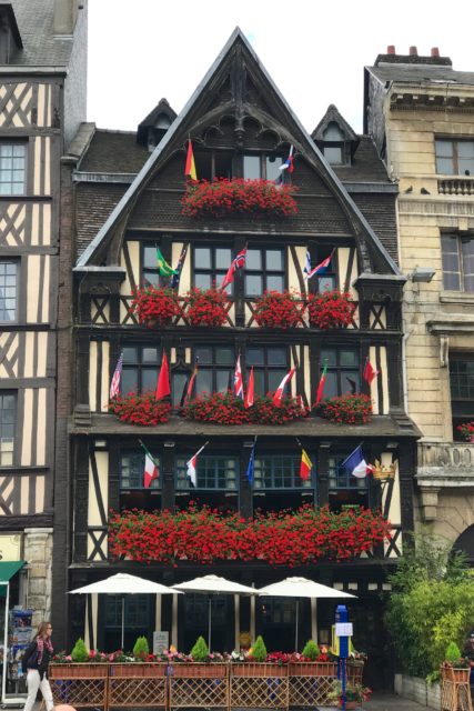Photo of the front of La Couronne, with flags and red flowers at its windows