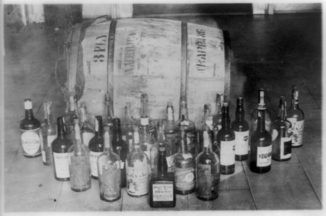 black and white photo of bottles in front of a whiskey barrel