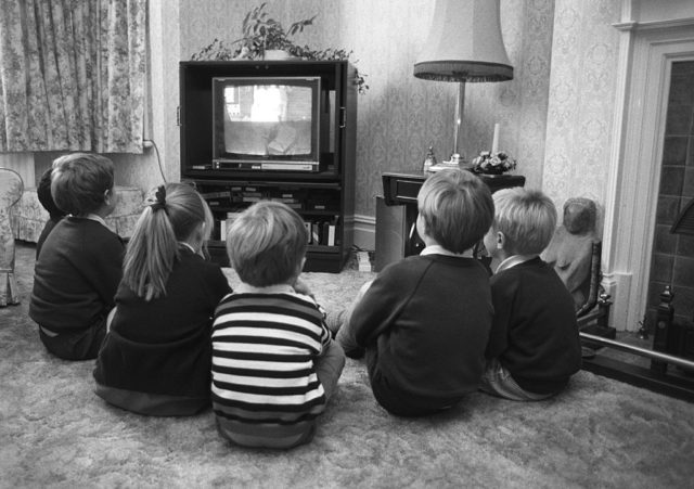 Children sit on the ground in front of a TV.