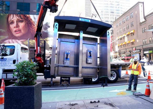 a payphone is lifted onto a truck in a busy NYC intersection