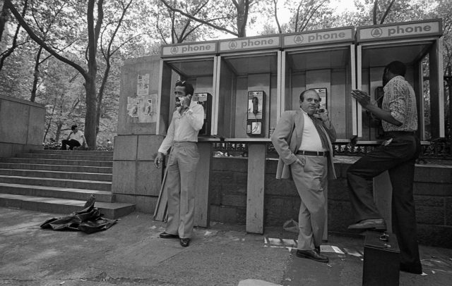 Black and white photo of 3 men using public payphones 