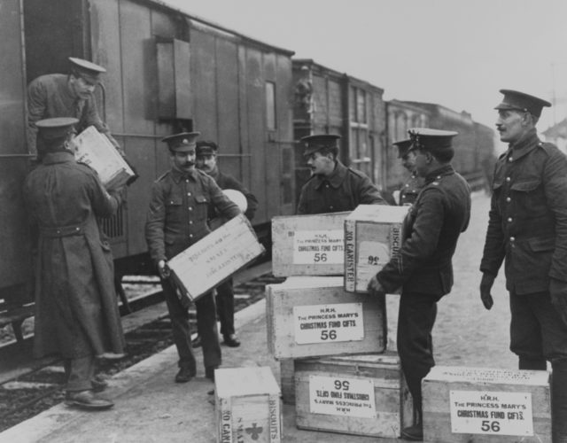 Black and white image of men hauling boxes of Princess Mary's Christmas gift off of a train