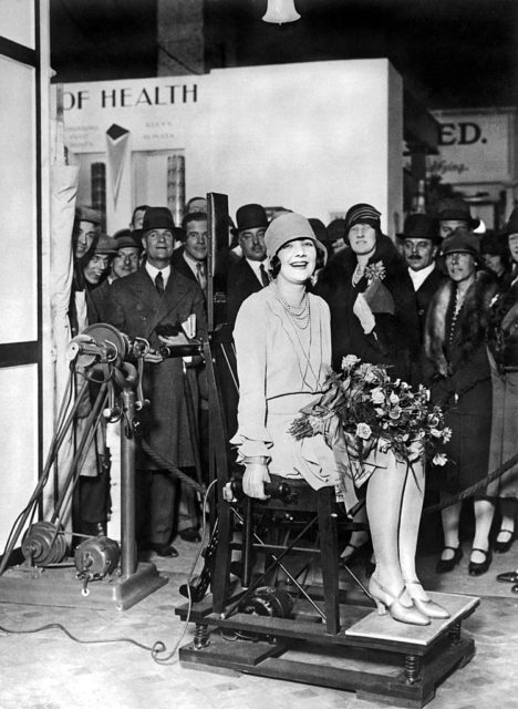 A woman sits on a vibrotherapy chair in front of a crowd at the New Health Exhibition in London, England in 1927.