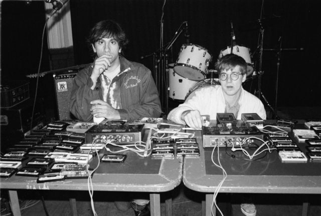 Two men at a table covered in cassette tapes