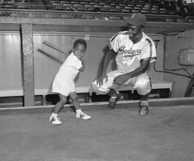 Two-and-a-half-year-old Jackie Robinson Jr. shows his famous dad, Jackie Robinson Sr., how to slice at the ball. (Photo Credit: Bettmann / Getty Images)