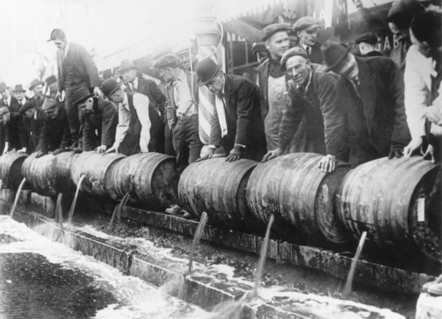 Black and white photo of authorities dumping alcohol from barrels into the sewers