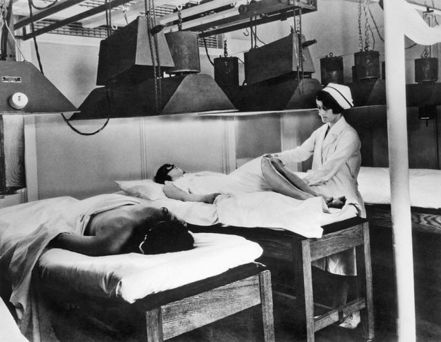 Two women lie on tables under large lamps for artificial sun baths at the Kellogg's sanitarium.