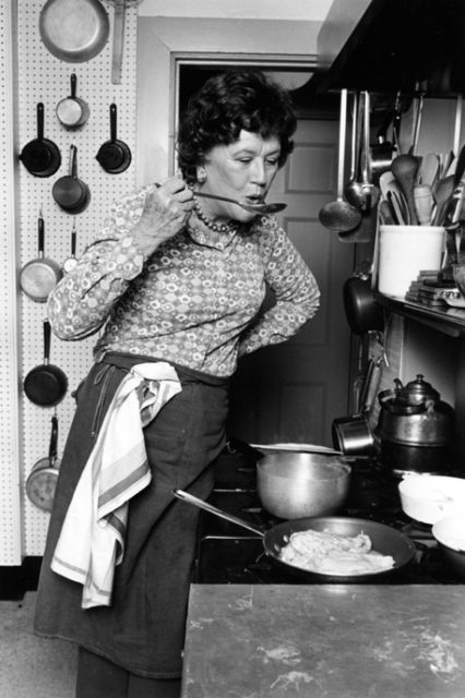 Black and white photo of Julia Childs taking a taste of a soup