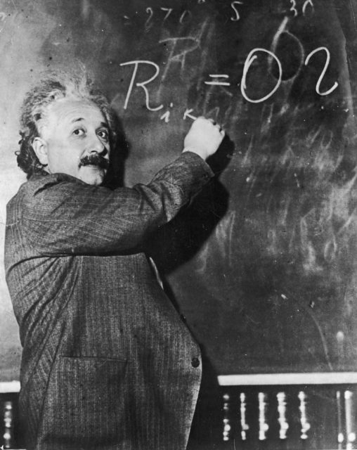 Einstein pointing to an equation on a blackboard