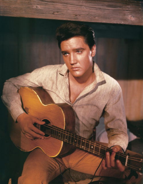 Elvis plays a guitar with a sad expression on his face