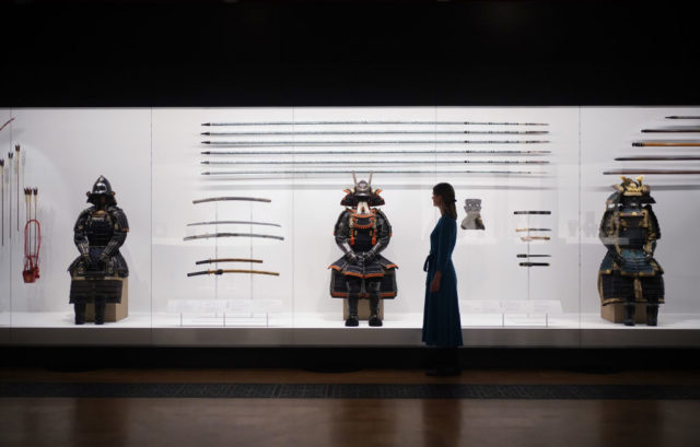 Woman walking in front of samurai armor and weapons on display