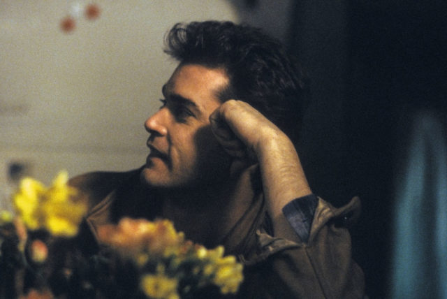 Young Ray Liotta leans on his first on a table with flowers