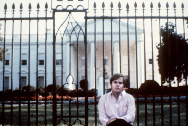 Hinckley sitting in front of the fence surrounding the White House.