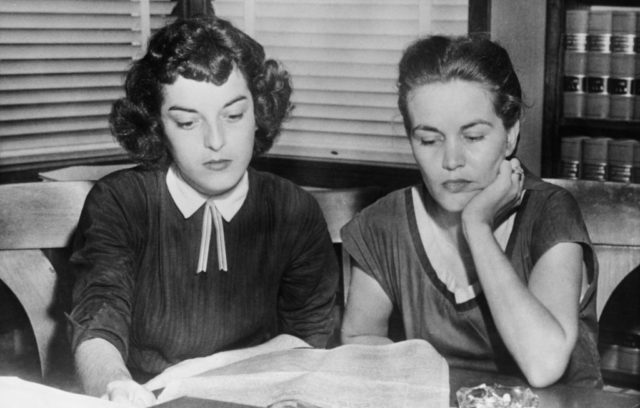 Black and white photo of two women sitting staring at a newspaper.