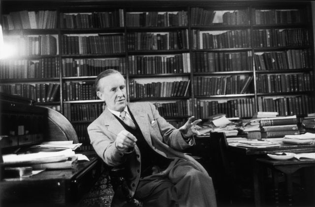 Black and white photo of J.R.R. Tolkien sitting in front of a large book shelf