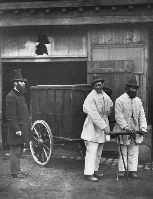 Two men pull a cart while disinfecting the streets of Victorian London