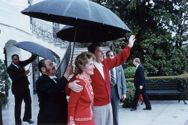 Ronald Reagan and Nancy Reagan smile for photos under an umbrella.