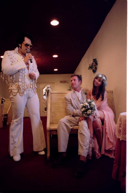 Elvis impersonator speaking to two newly weds sitting in pew
