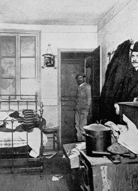 Black and white image of a man standing in Vincenzo Perugia's room in Paris.