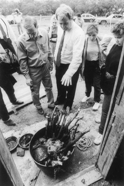 Black and white photo of people standing around a cauldron filled with sticks and bones.