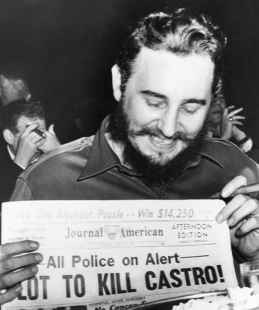 Black and white photo of Castro holding a newspaper with a headline about assassination attempts against him.