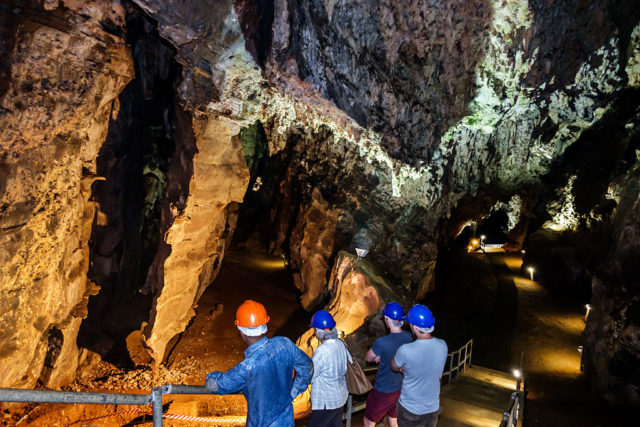 Coloured photo of people wearing construction helmets walking inside a cave system with tall ceilings.