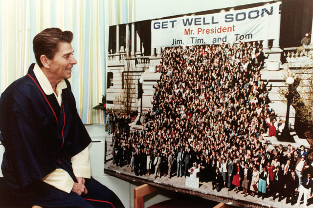 Ronald Reagan looks at a large photograph that reads "Get Well Soon, Mr. President"
