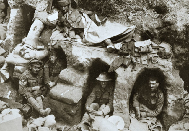 Black and white photo of soldiers sitting inside holes in a wall dug by German soldiers.