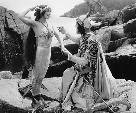 Black and white photo of a woman in a mermaid costume with a man wearing Roman armour.