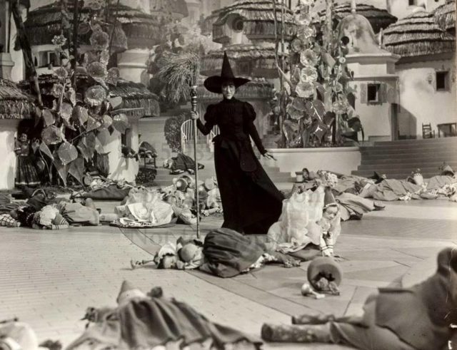 Black and white photo of the Wicked Witch of the West standing in the middle of Munchkinland