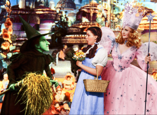 Coloured photo from the Wizard of Oz, Wicked Witch of the West, Dorothy, and the Good Witch standing together.