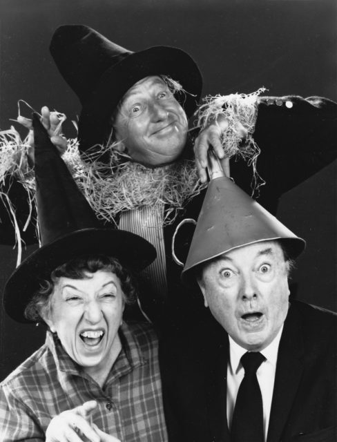 Black and white photo of Margaret Hamilton and two other cast members smiling together wearing costume hats.