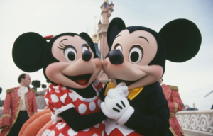 Colored photo of Mickey and Minnie Mouse holding hands in front of a castle at Disneyland Paris.