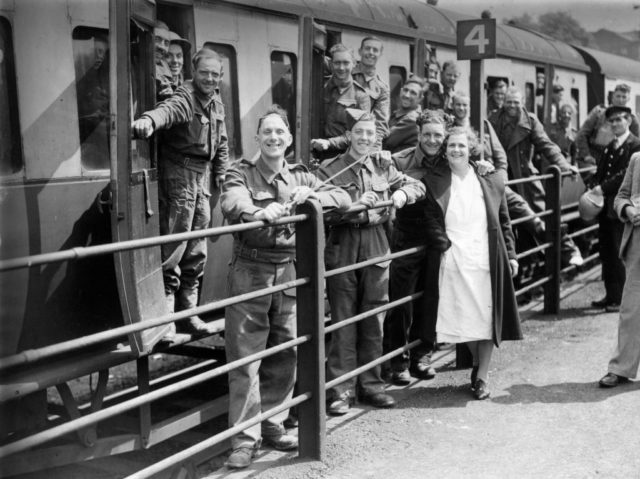 Black and white photo of soldiers getting off a train smiling at the camera alongside civilians.