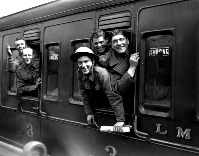 Black and white photo of smiling men in military uniform leaning out a train window.