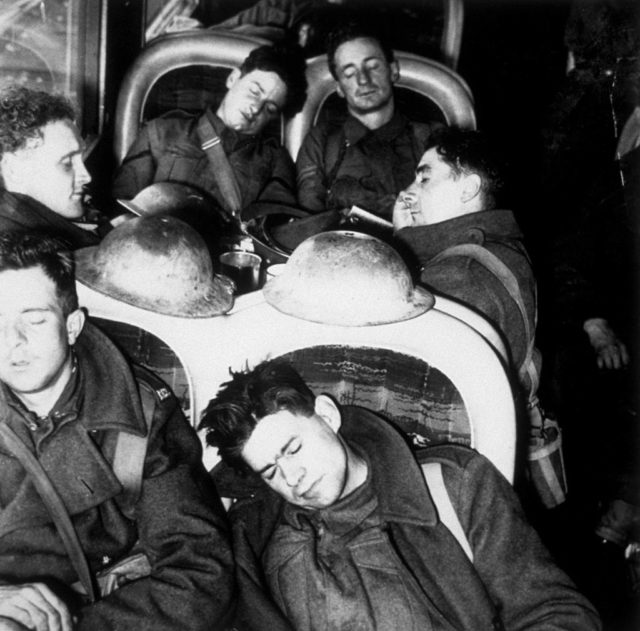 Black and white photo of men in military uniform sleeping on a train.