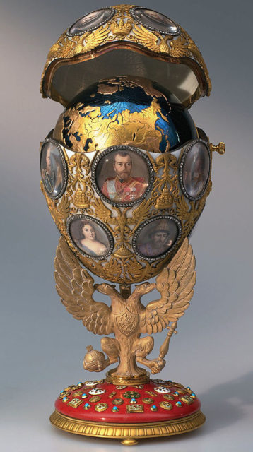 Coloured photo of a Romanov Faberge egg. It is gold with pictures of the family on the front, and the top opens to show a gold and blue globe.