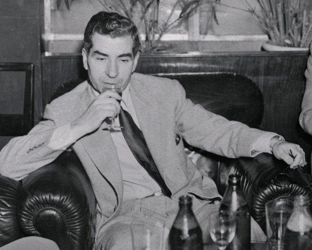 Mobster Lucky Luciano drinks wine while seated in a leather armchair