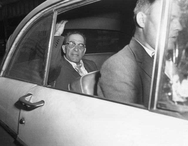 Mob boss Vito Genovese waves from the backseat of a car after posting bail