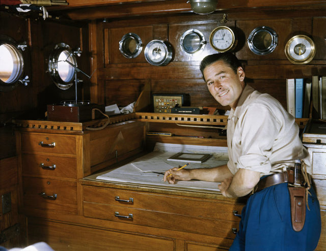 Errol Flynn looks over maps while inside the cabin on his yacht