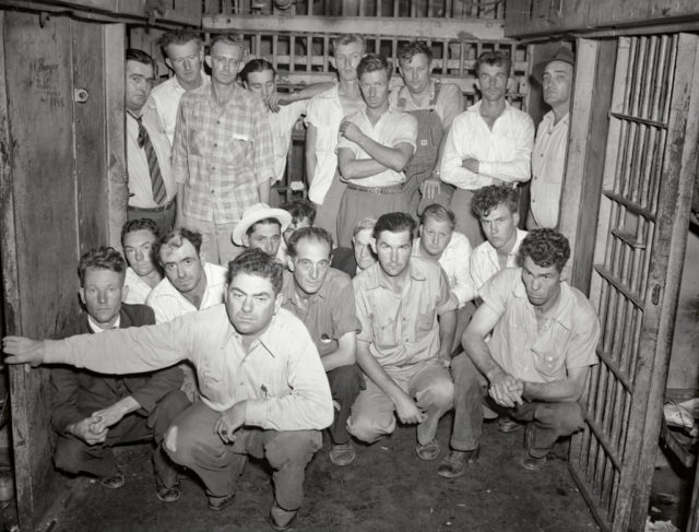 Black and white photo of a group of men, some standing and some kneeling, in a jail.