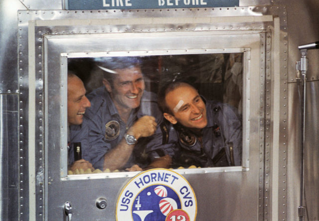 Apollo 12 astronauts gin from the window of their Mobile Quarantine Facility