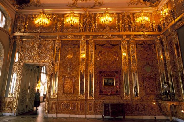 Coloured photo of the Amber Room, a room with tall ceilings with ornate amber and gold detailing throughout the room.
