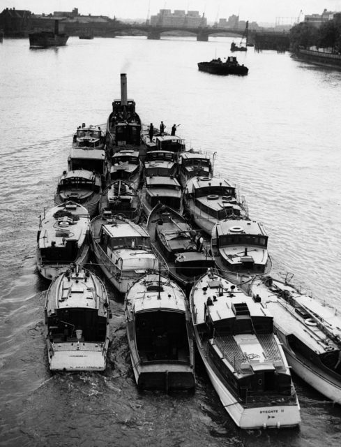 Black and white photo of small boats being pulled by a large boat down the Thames River.